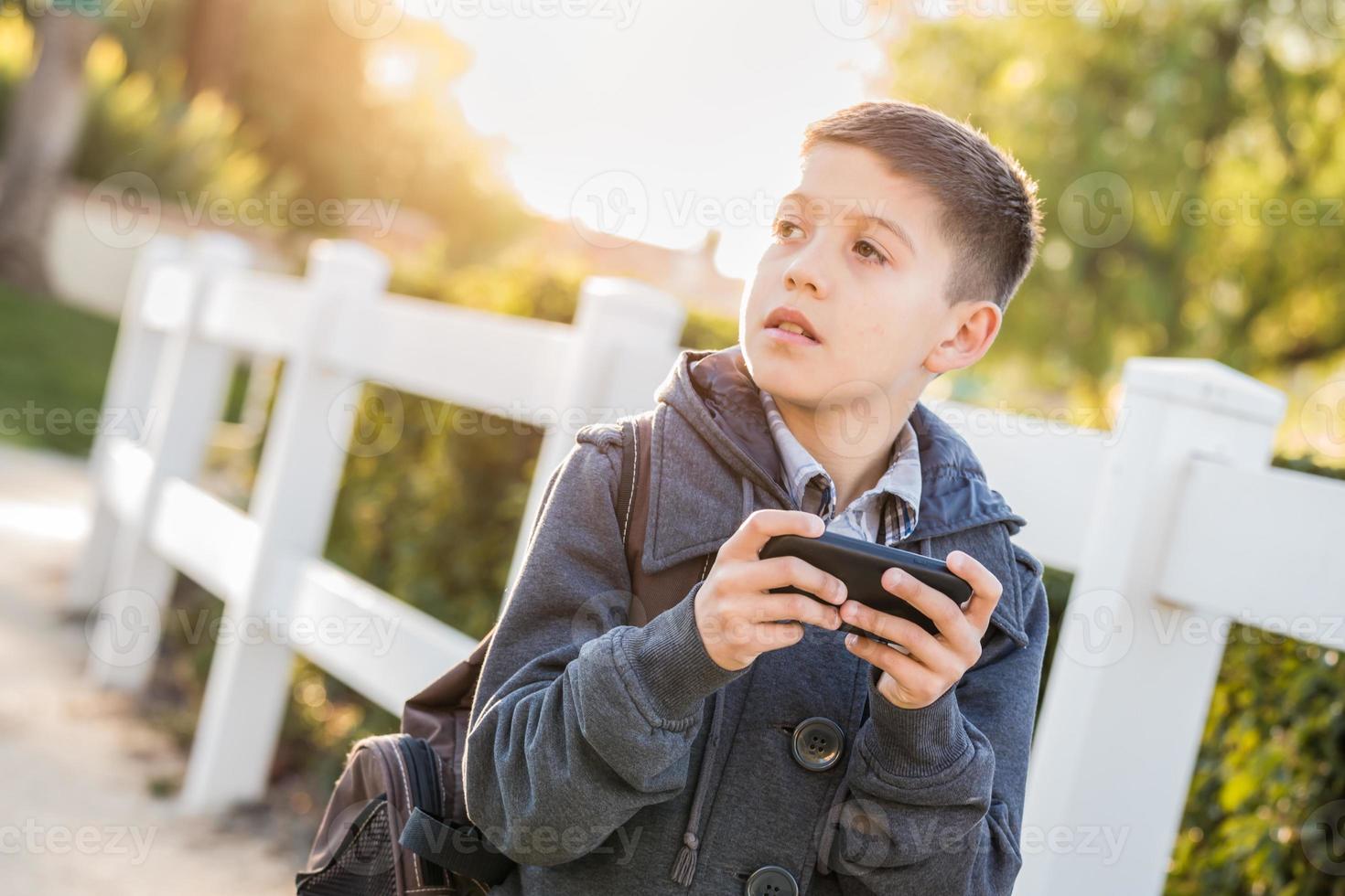 Concerned Young Hispanic Boy Walking With Backpack Holding Cell Phone photo