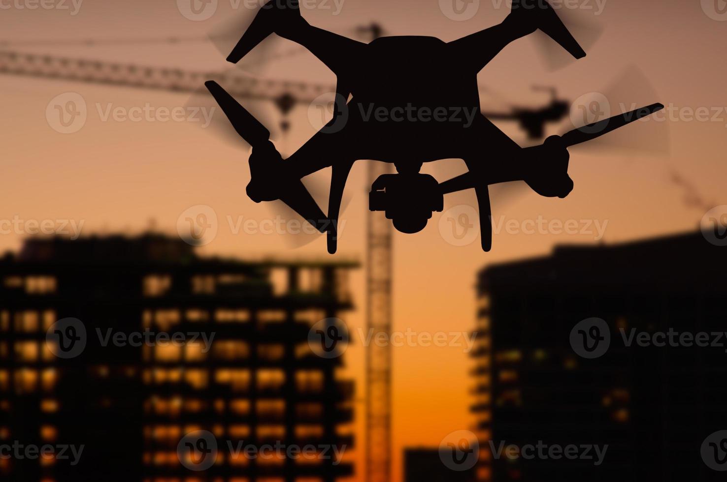 Silhouette of Unmanned Aircraft System Quadcopter Drone In The Air Over Buildings Under Construction. photo