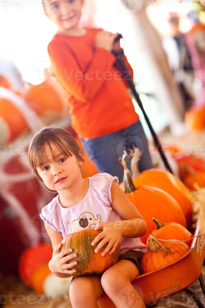 Cute Girl Riding Wagon with Her Pumpkin and Sister photo