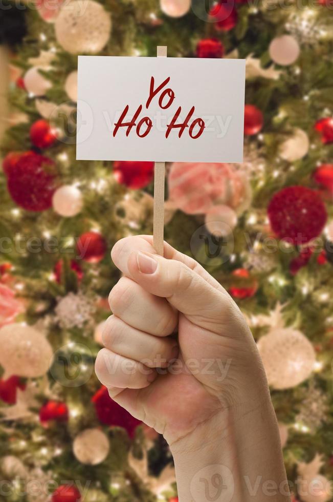 Hand Holding Yo Ho Ho Card In Front of Decorated Christmas Tree. photo