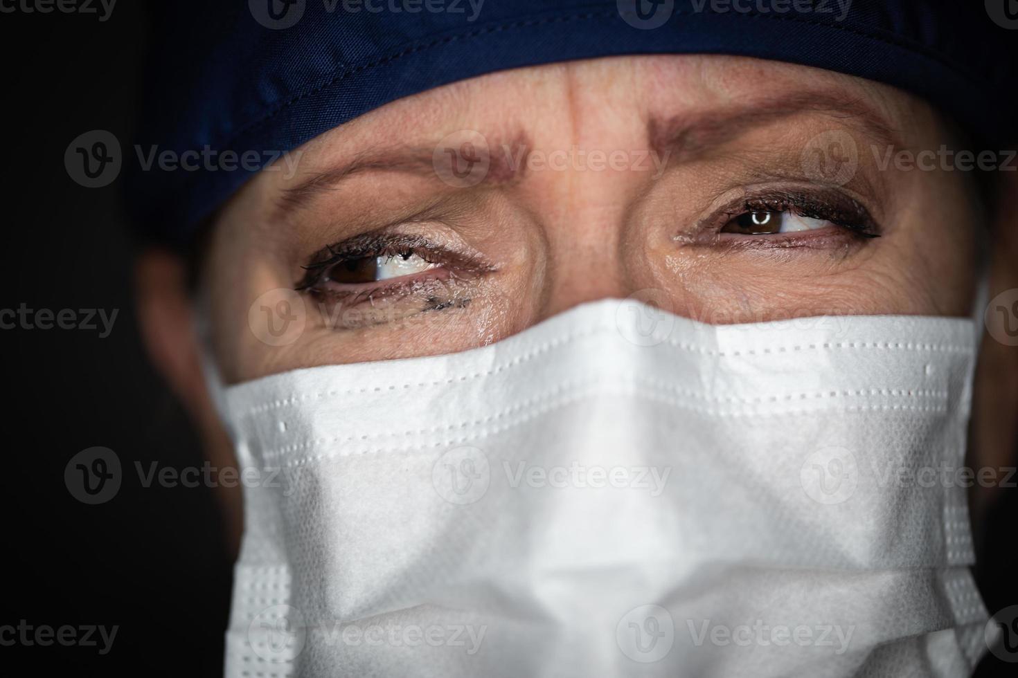 Tearful Stressed Female Doctor or Nurse Wearing Medical Face Mask on Dark Background photo