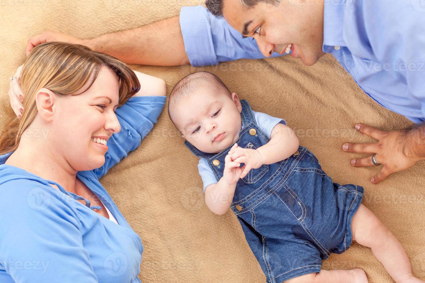 Young Mixed Race Couple Laying With Their Infant On A Blanket photo