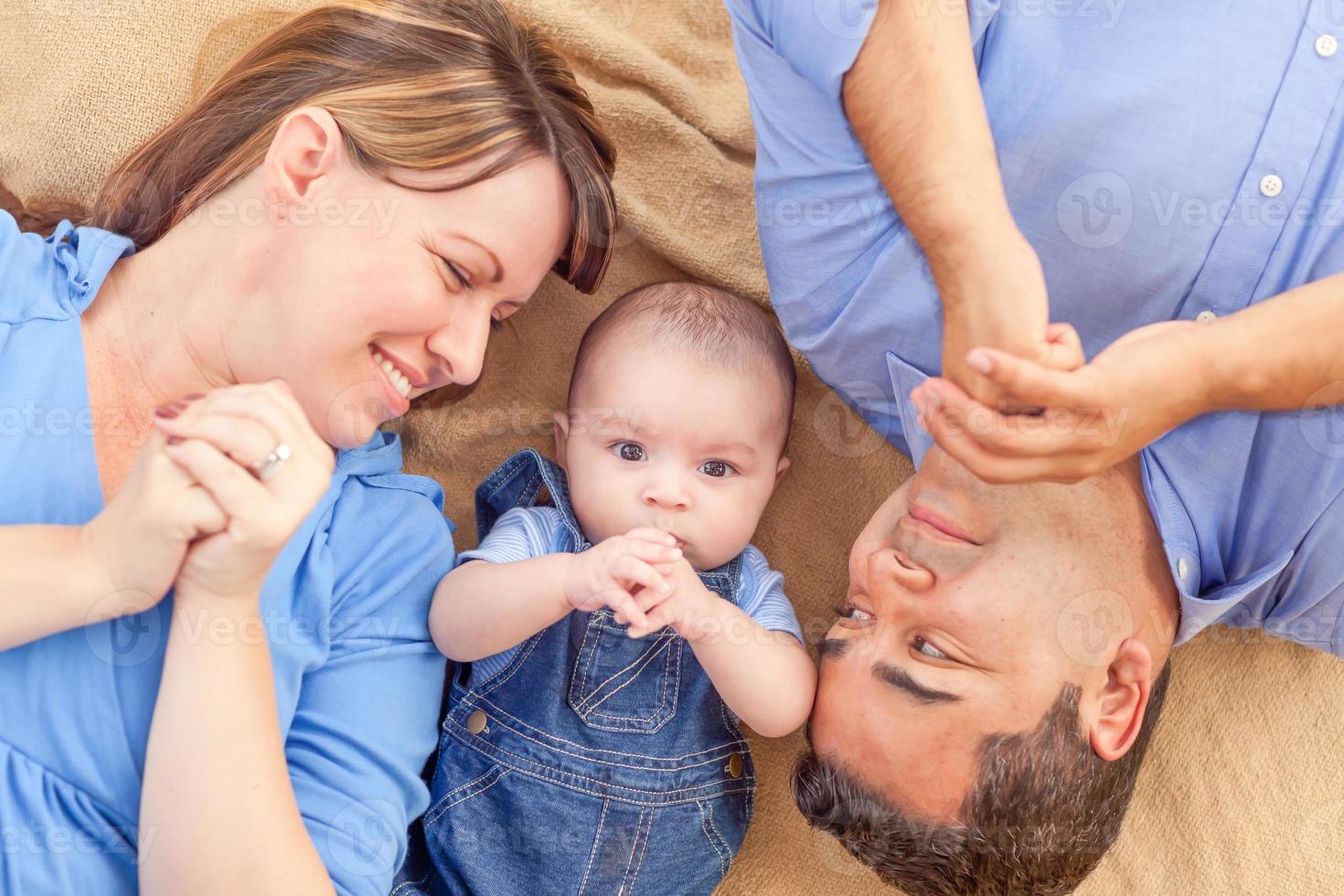 Young Mixed Race Couple Laying With Their Infant On A Blanket photo