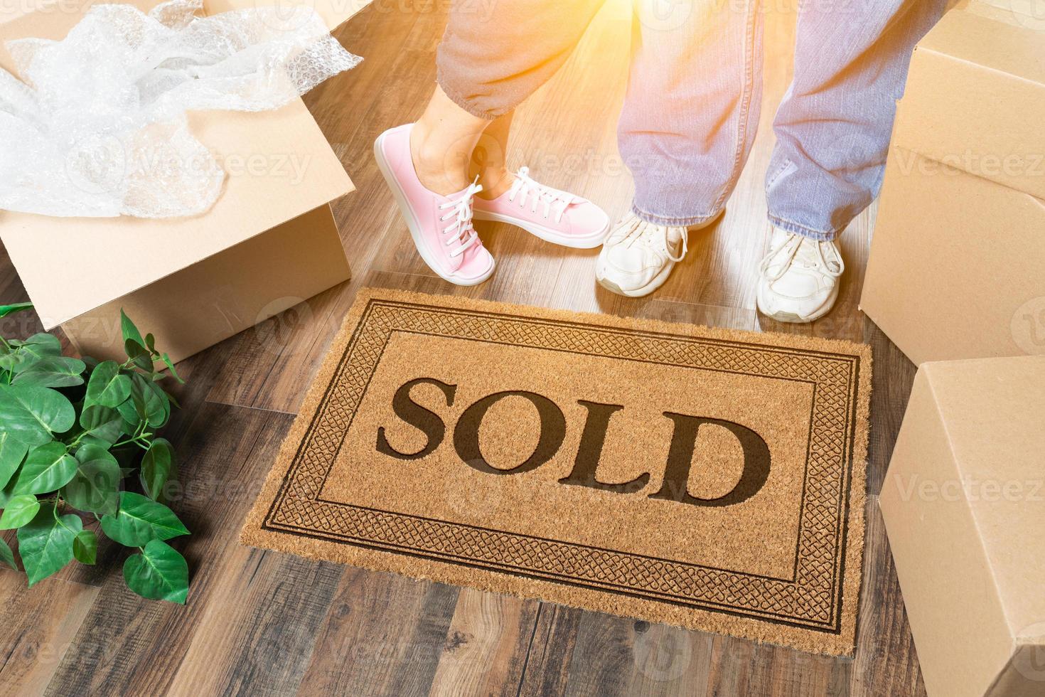 Man and Woman Standing Near Sold Welcome Mat, Moving Boxes and Plant photo