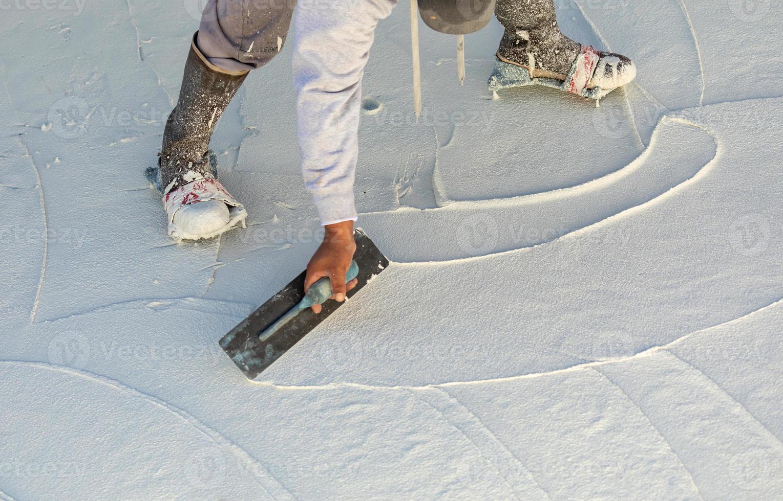 trabajador que usa zapatos con púas alisando el yeso húmedo de la piscina con una paleta foto