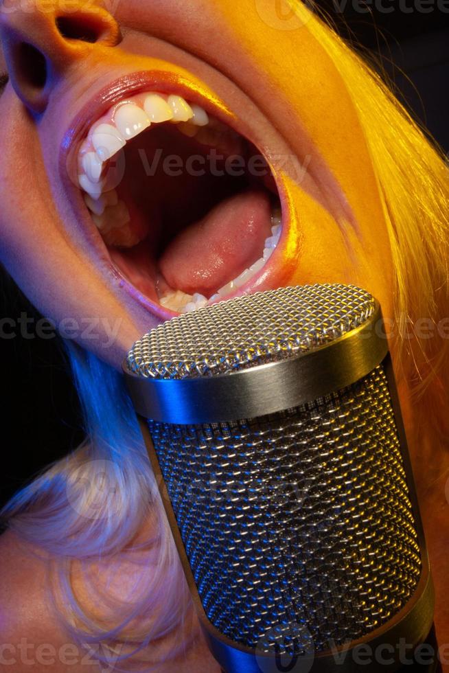 Female vocalist under gelled lighting sings with passion into condenser microphone. photo