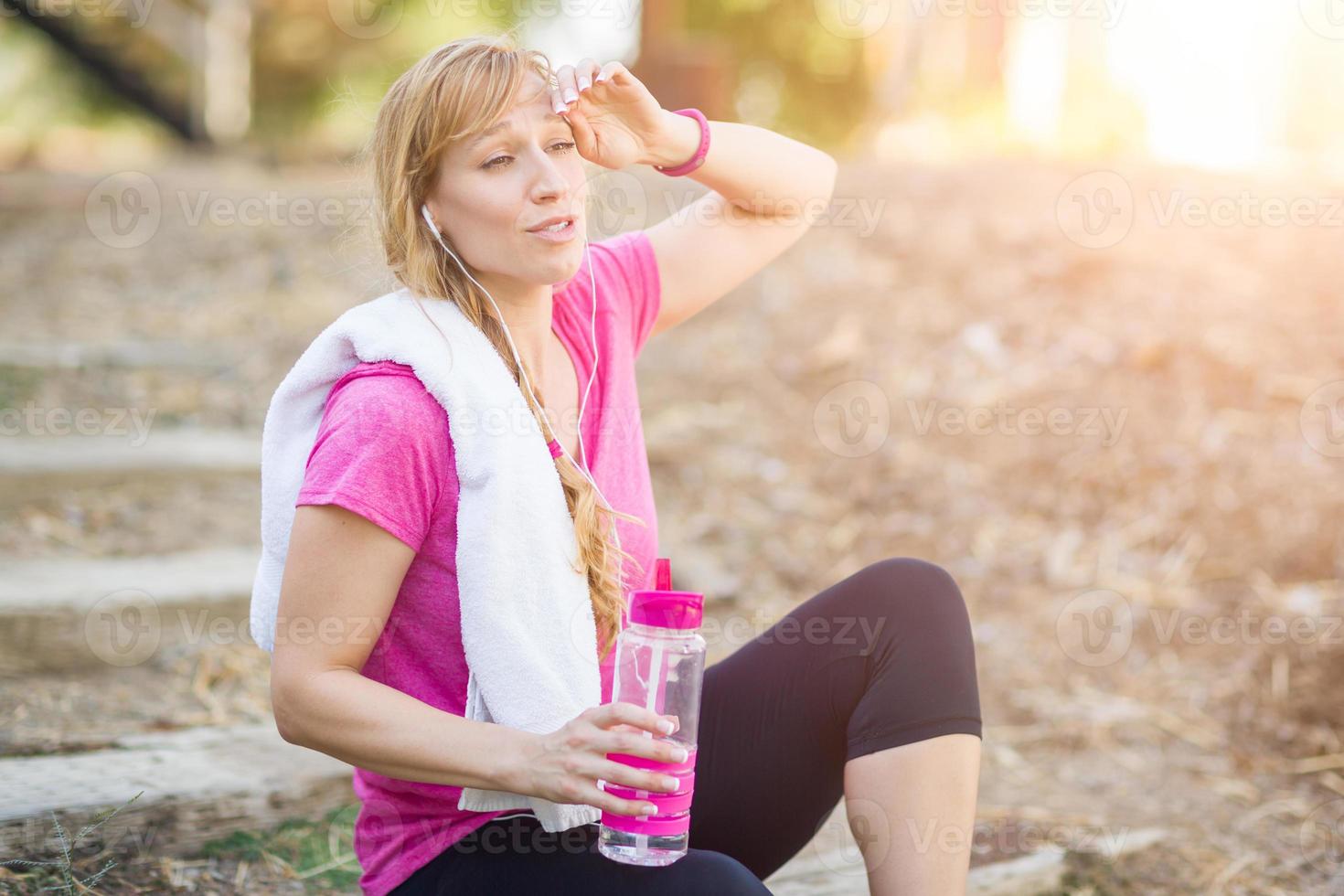 Young Fit Adult Woman Outdoors With Towel and Water Bottle in Workout Clothes Listening To Music with Earphones. photo