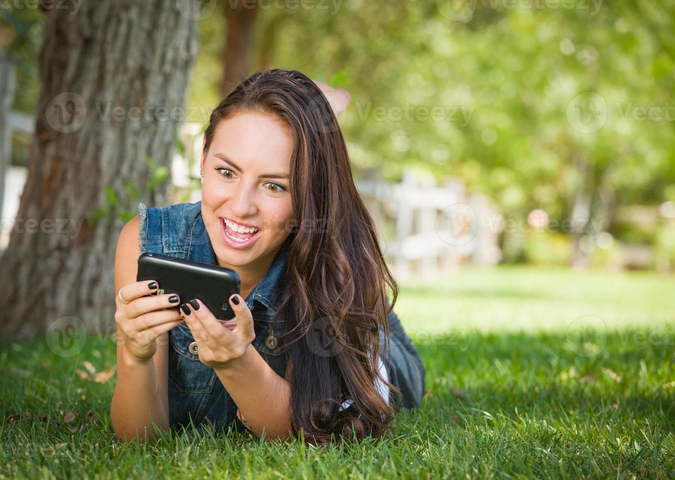 Shocked Mixed Race Young Female Texting on Her Cell Phone Outside Laying in the Grass photo
