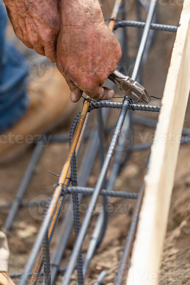 Worker Securing Steel Rebar Framing With Wire Plier Cutter Tool At Construction Site photo