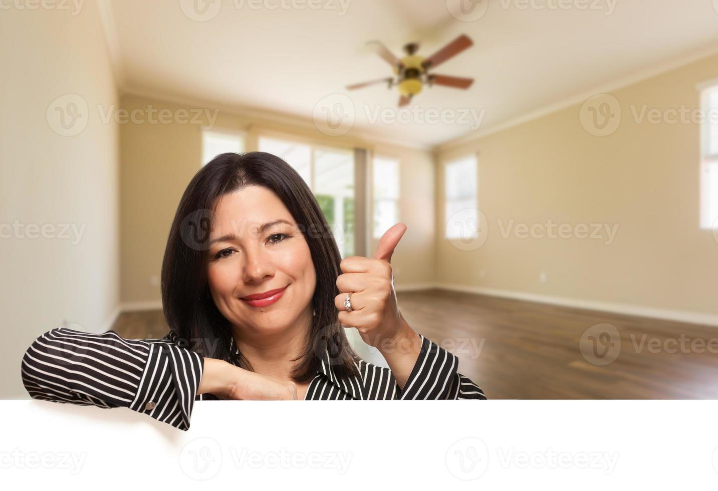 Hispanic Woman with Thumbs Up In Empty Room of House photo