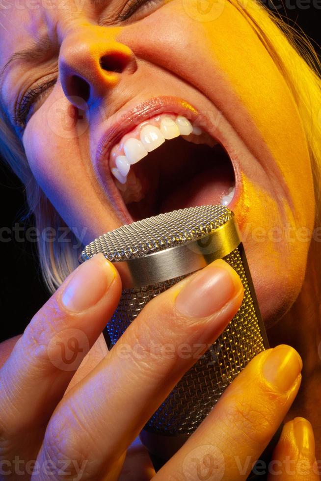 Female vocalist under gelled lighting sings with passion into condenser microphone. photo