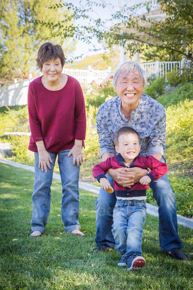 abuelos chinos felices divirtiéndose con su nieto de raza mixta afuera foto