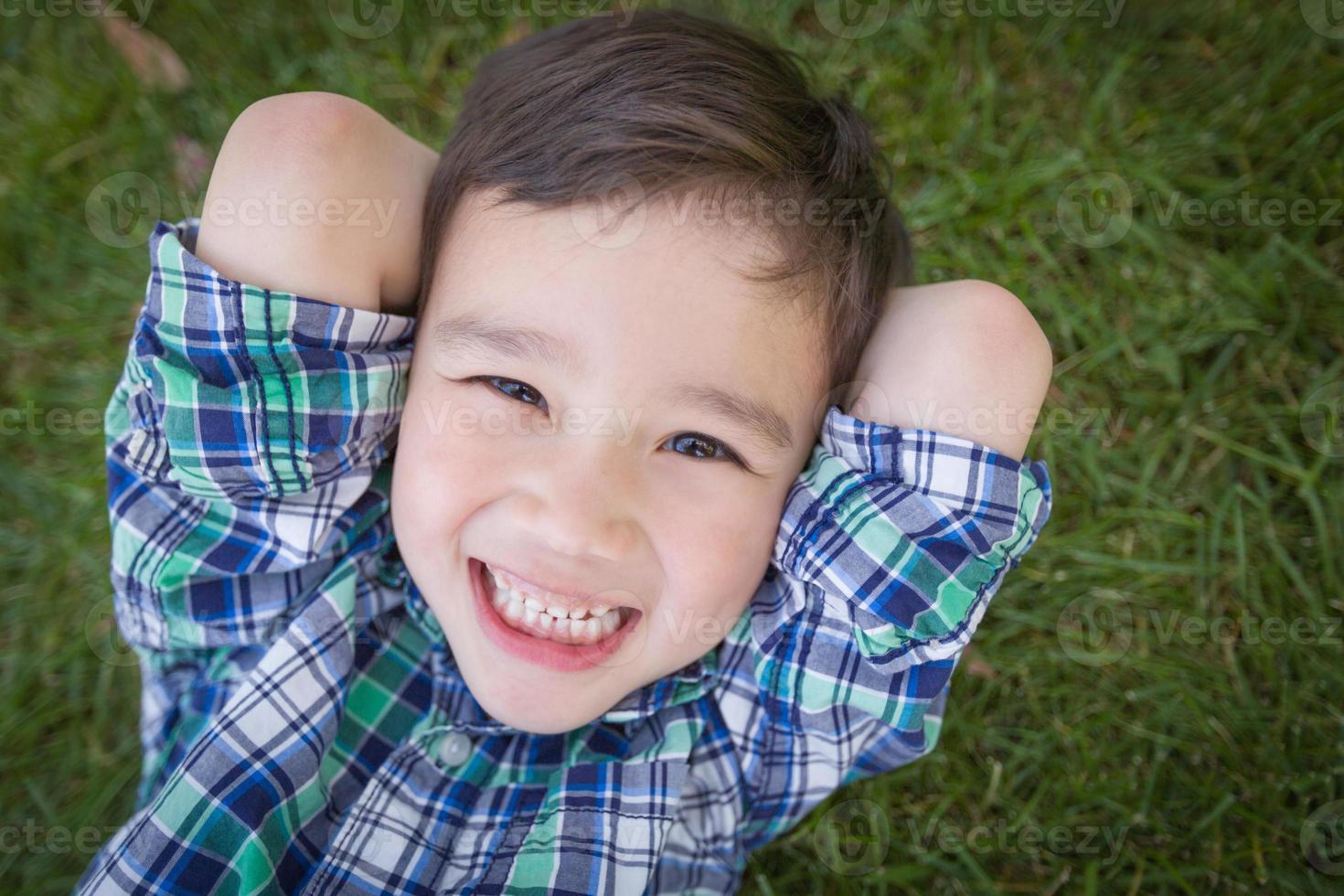 Mixed Race Chinese and Caucasian Young Boy Relaxing On His Back Outside On The Grass photo