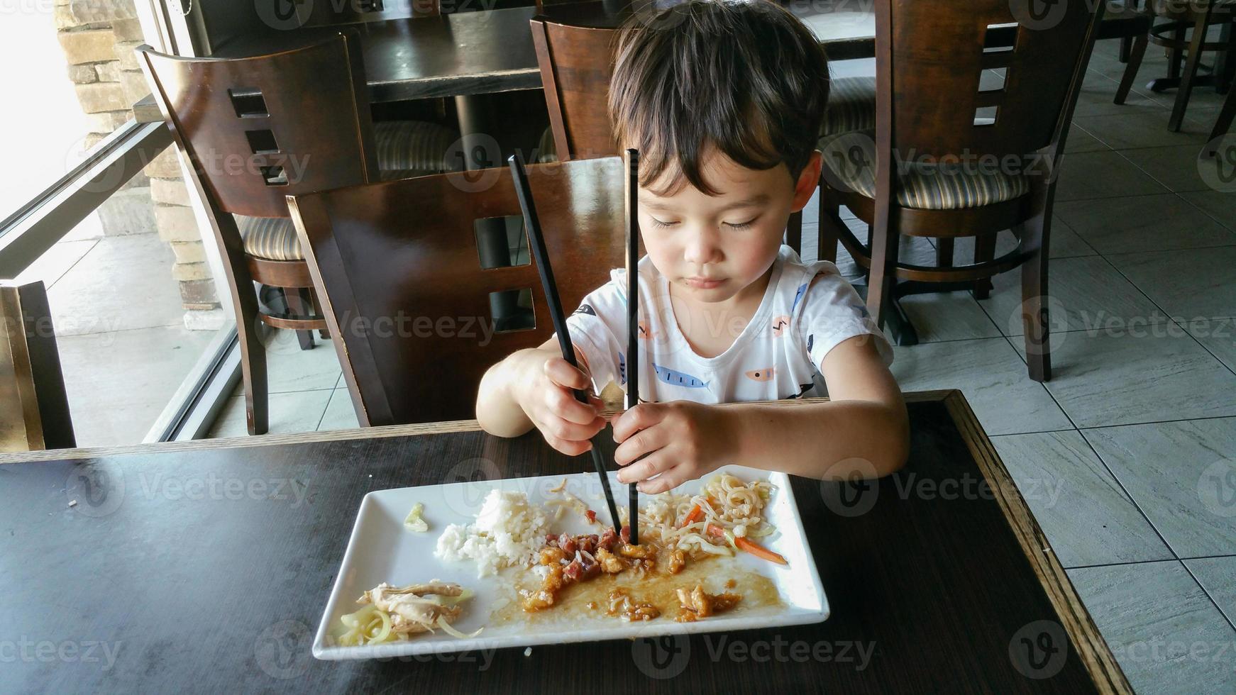 lindo joven chino y caucásico aprendiendo a usar palillos en el restaurante foto