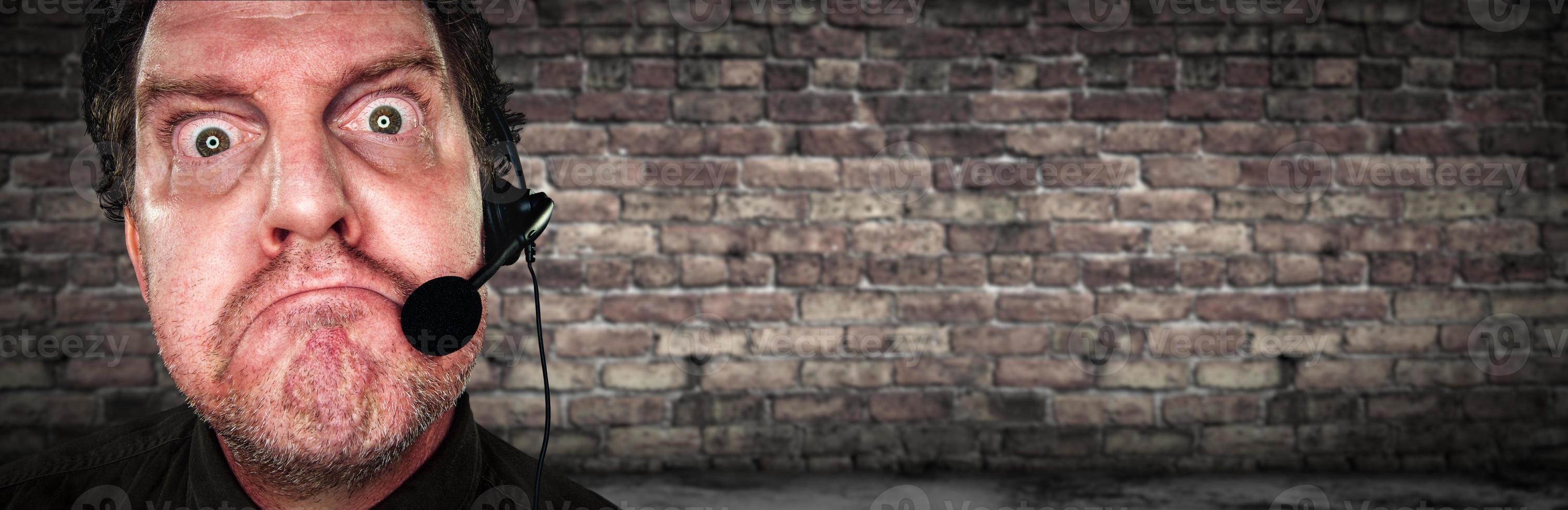Grumpy Businessman with Frowning Face Wearing Phone Headset In Office with Brick Background Banner photo