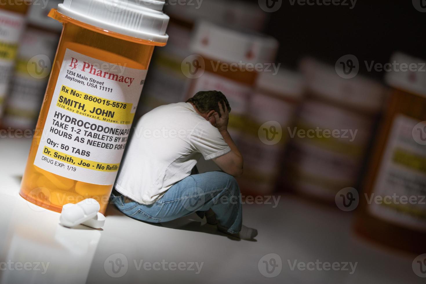 Man Holding Head Sitting Next To Hydrocodeon Pills and Bottle photo