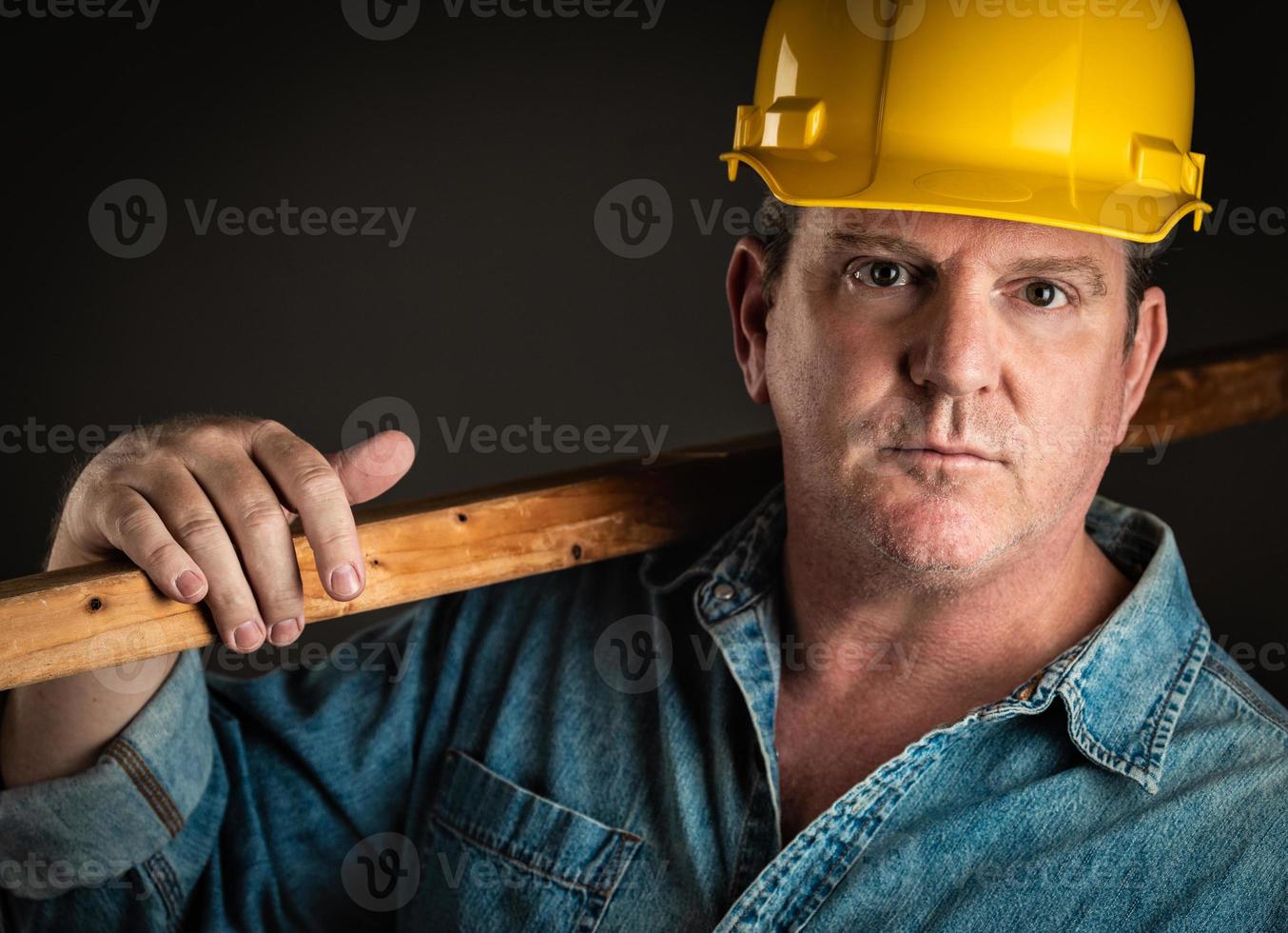 Serious Contractor in Hard Hat Holding Plank of Wood With Dramatic Lighting. photo