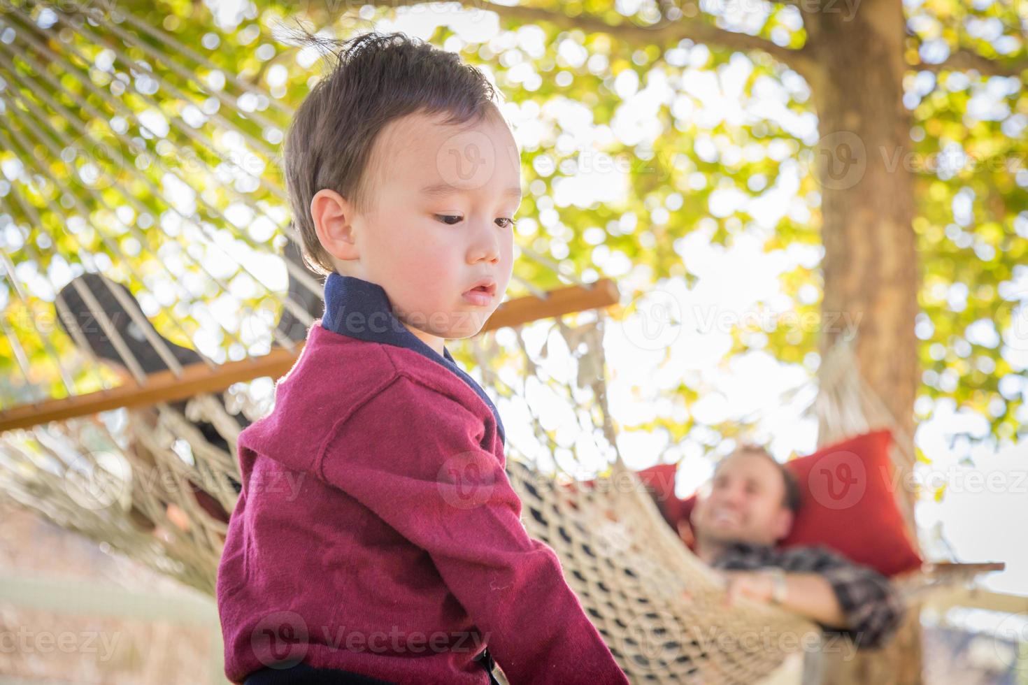 Mixed Race Boy Having Fun Outside While Parent Watches From Behind in a Hammock photo