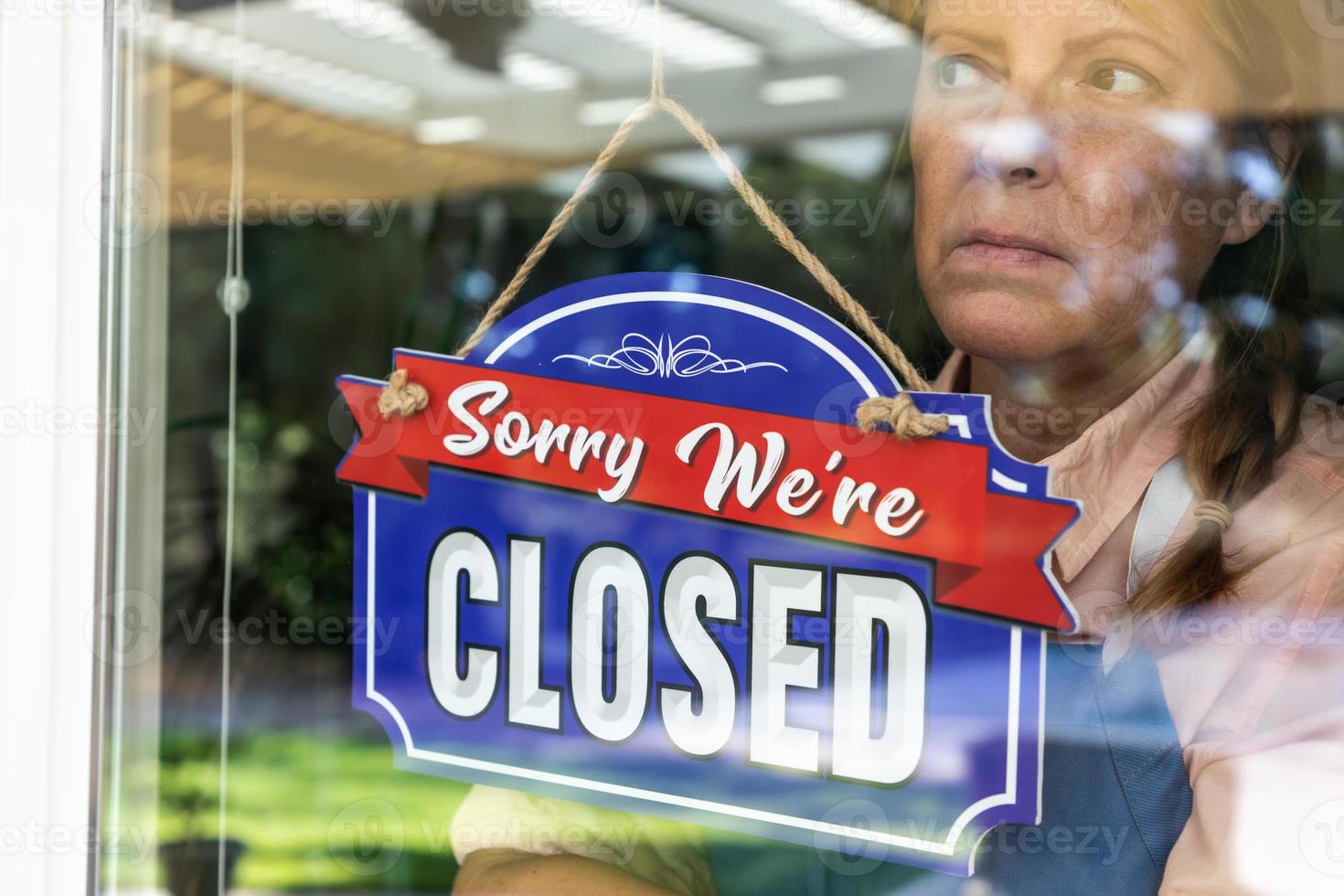 Sad Female Store Owner Turning Sign to Closed in Window photo