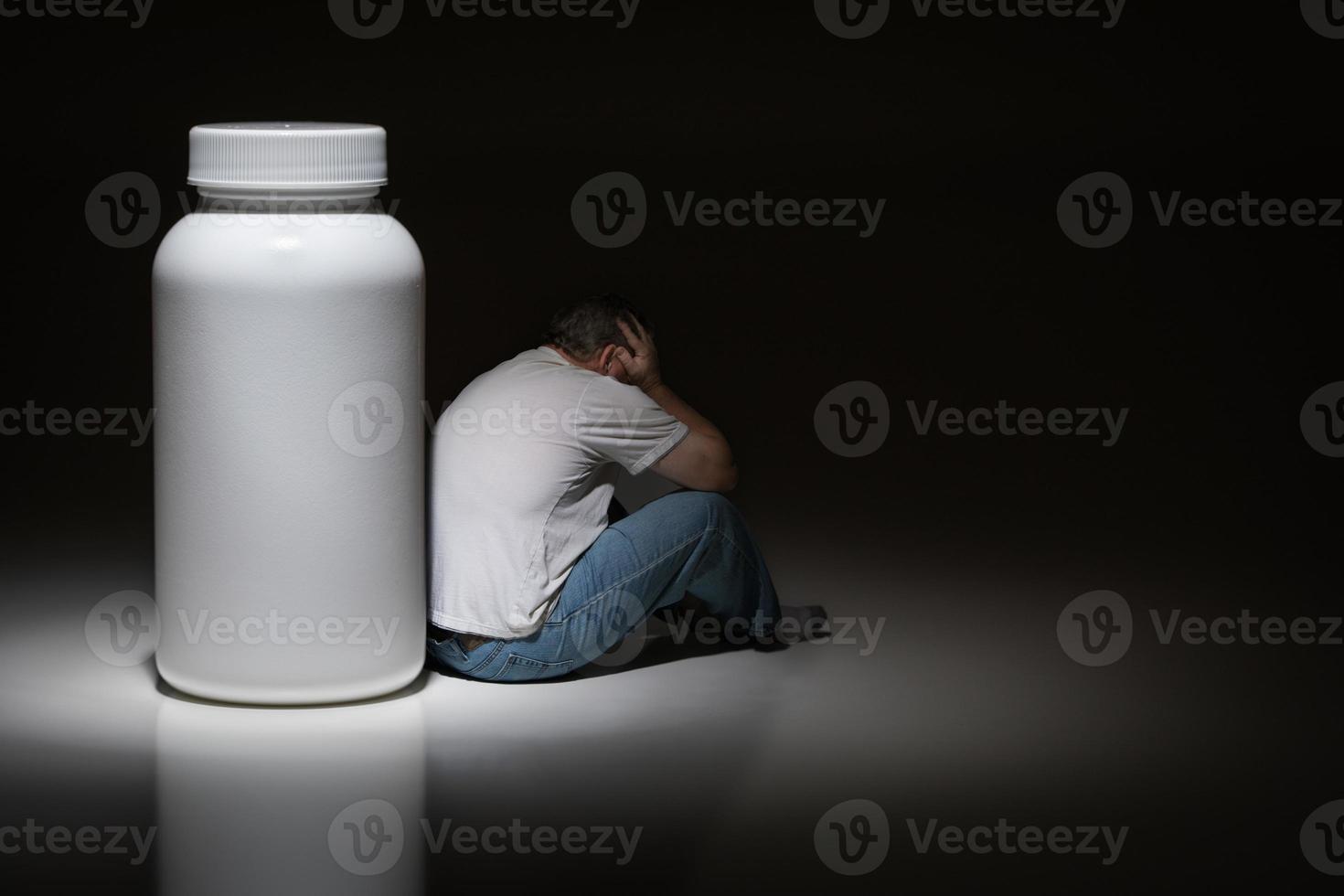 Man Holding Head Sitting Next To Blank Medication Bottle photo