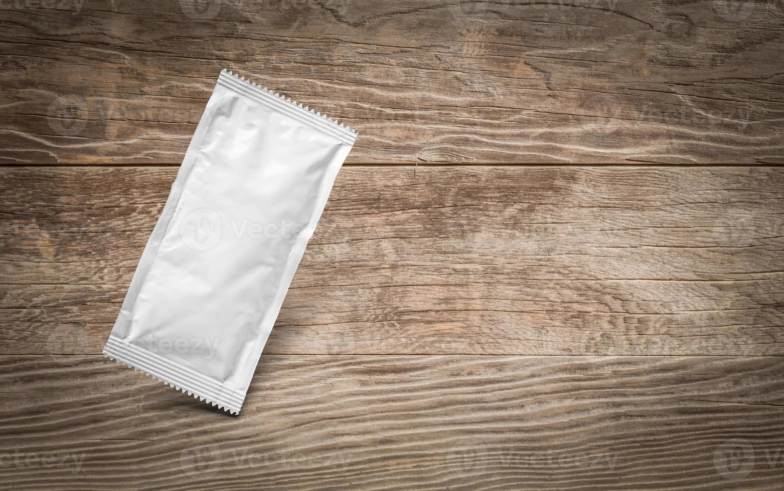 Blank White Condiment Packet Floating on Aged Wood Background photo