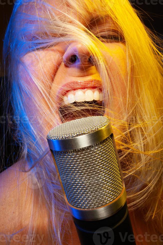 Female vocalist under gelled lighting sings with passion into condenser microphone. photo