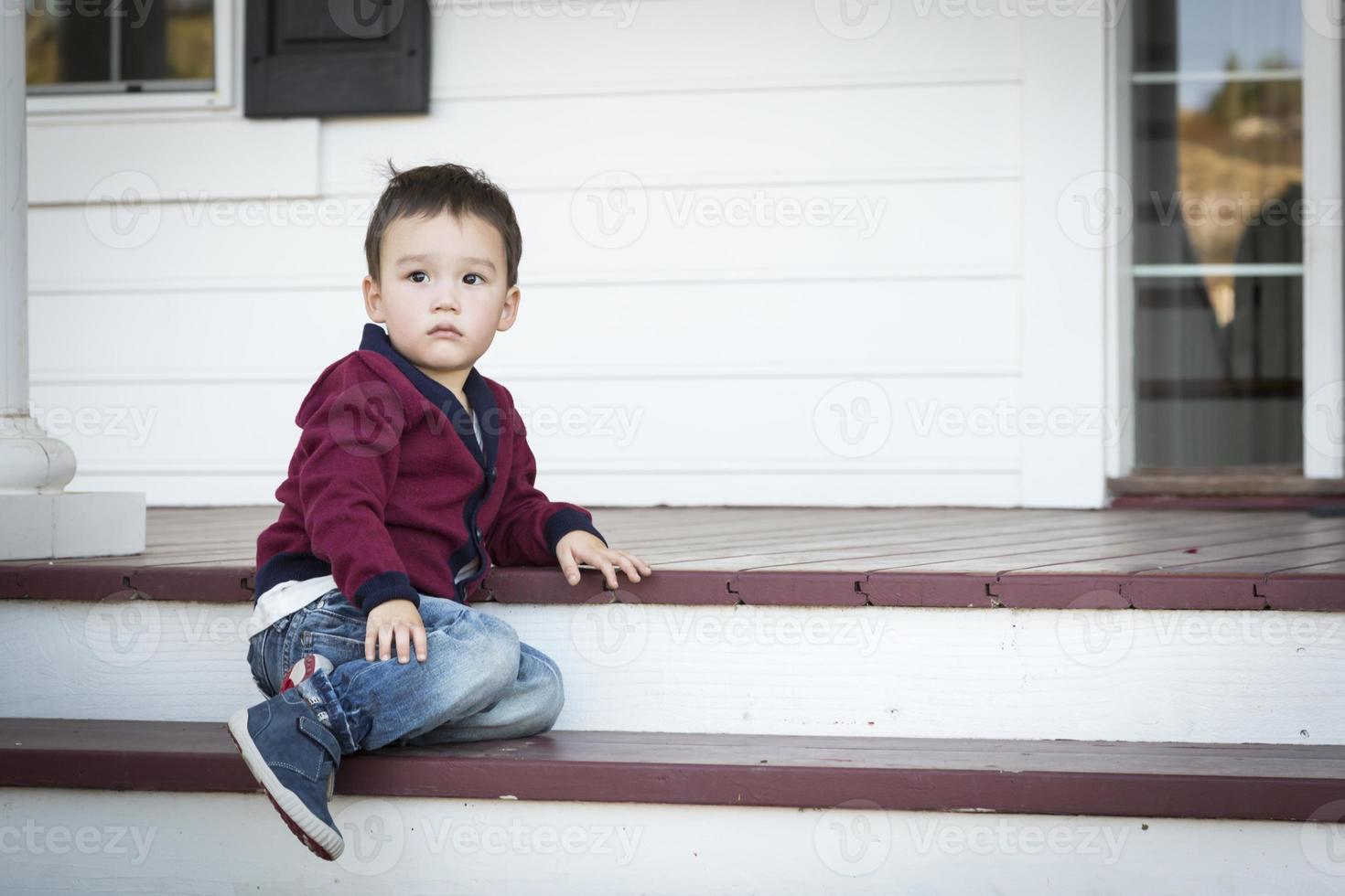 Melancholy Mixed Race Boy Sitting on Front Porch Steps photo