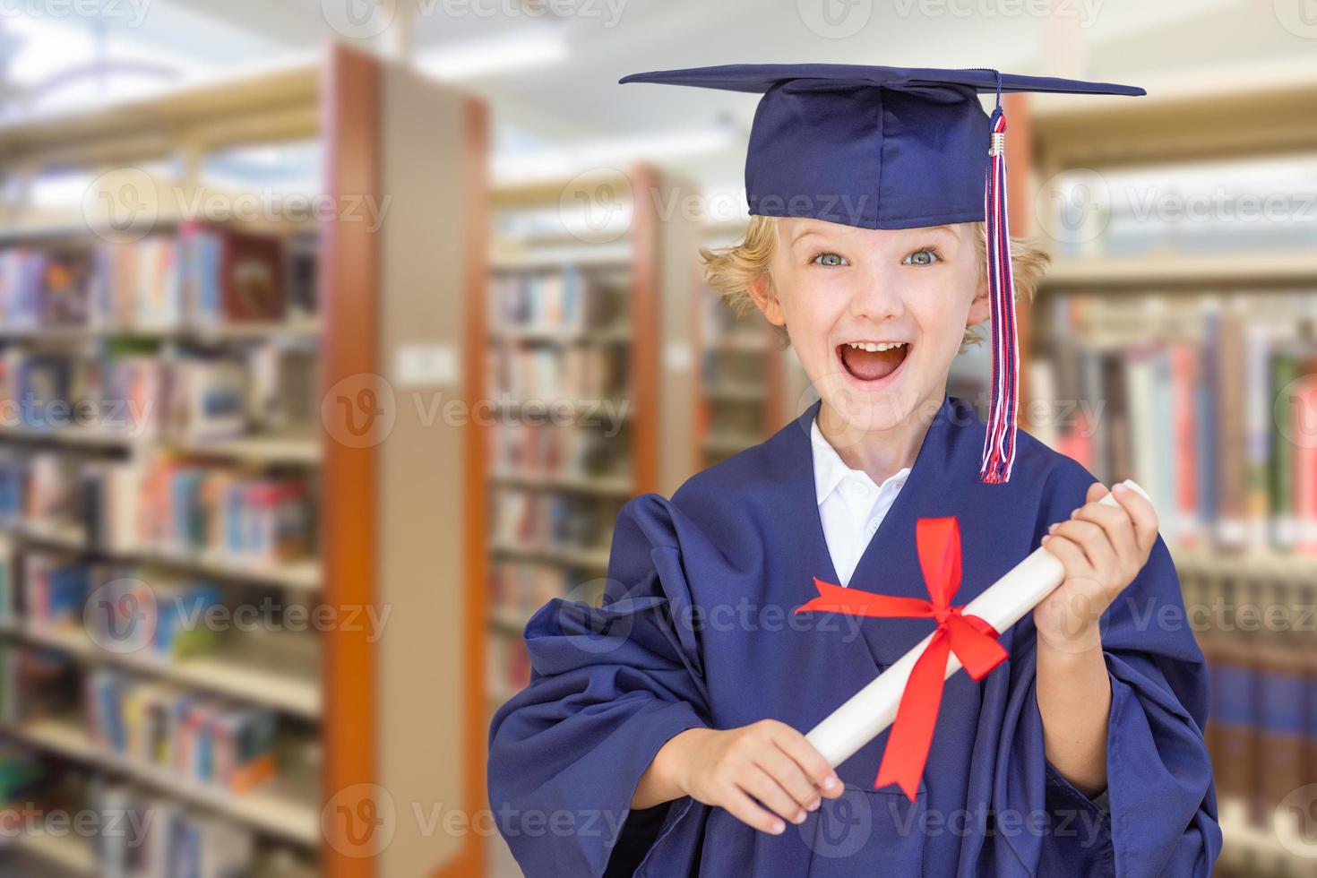 Cute Young Caucasian Boy Wearing Graduation Cap and Gown in The Library photo