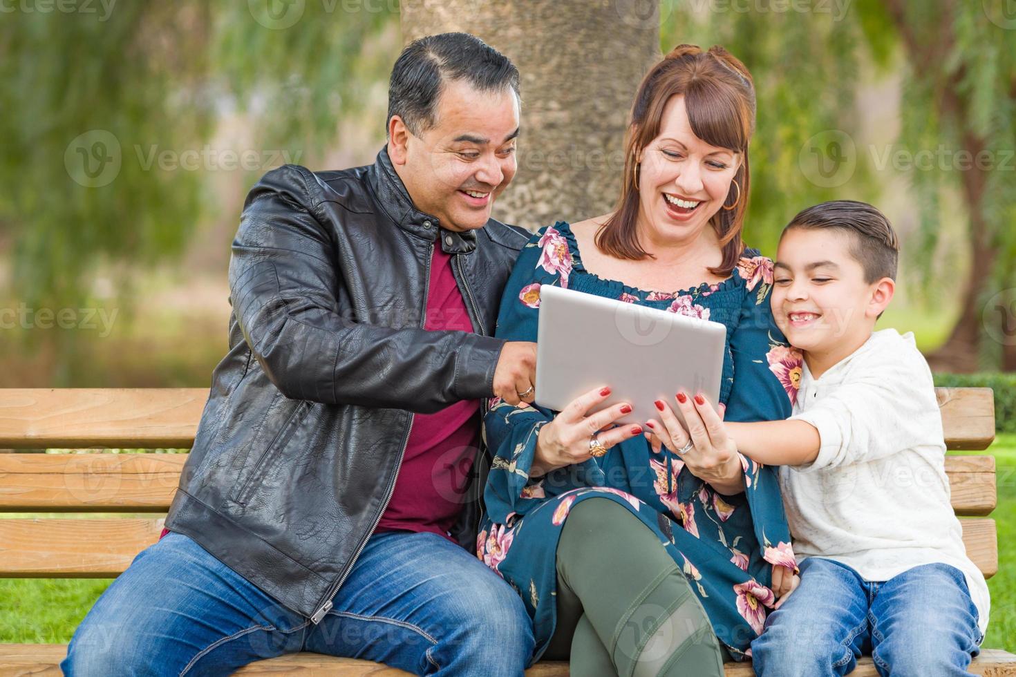 Caucasian Mother and Hispanic Father Using Computer Tablet With Mixed Race Son Outdoors photo