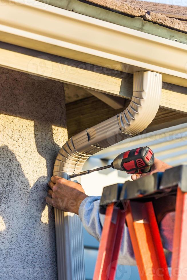 Worker Attaching Aluminum Rain Gutter and Down Spout to Fascia of House photo