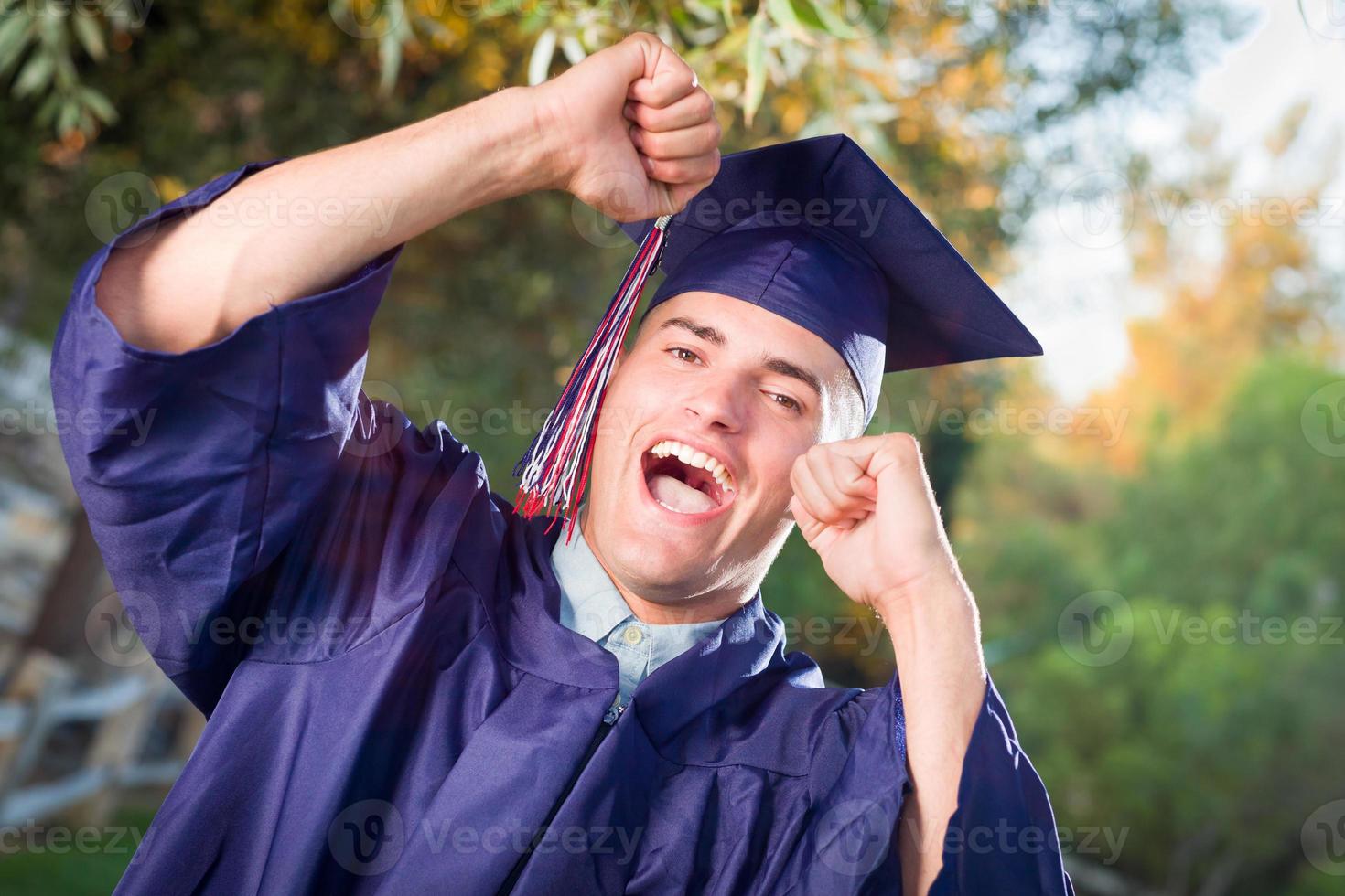 Happy Handsome Male Graduate in Cap and Gown Outside. photo