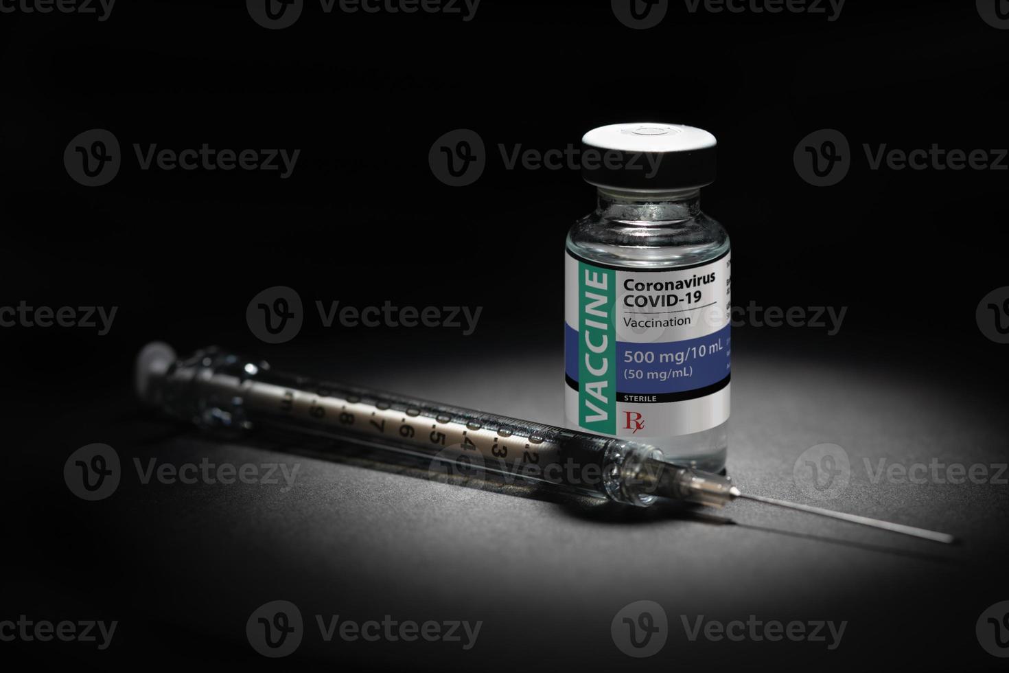 Syringe Needle and Coronavirus COVID-19 Vaccine Vial Spot Lit on Dark Background photo