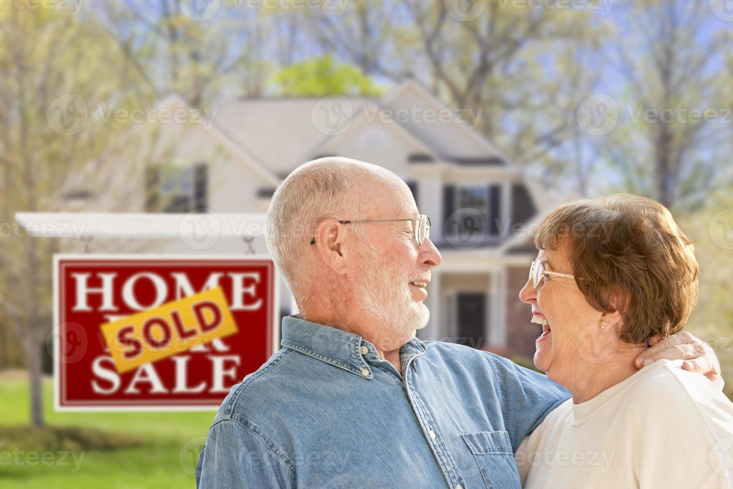Senior Couple in Front of Sold Real Estate Sign and House photo
