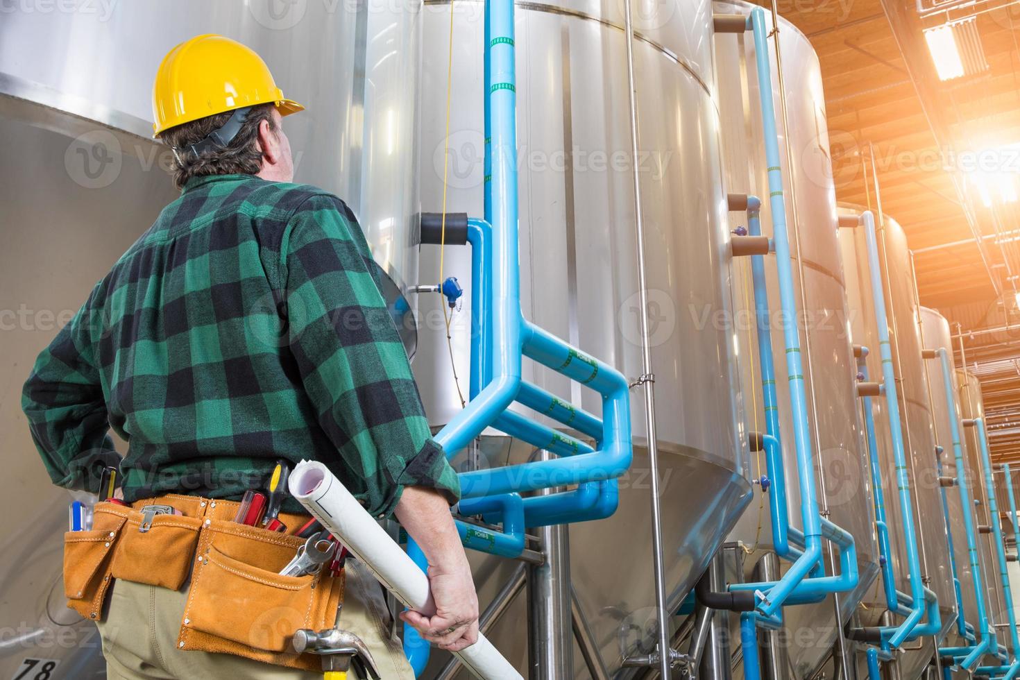 Man Wearing Hard Hat Looking Up At Large Industrial Tanks photo