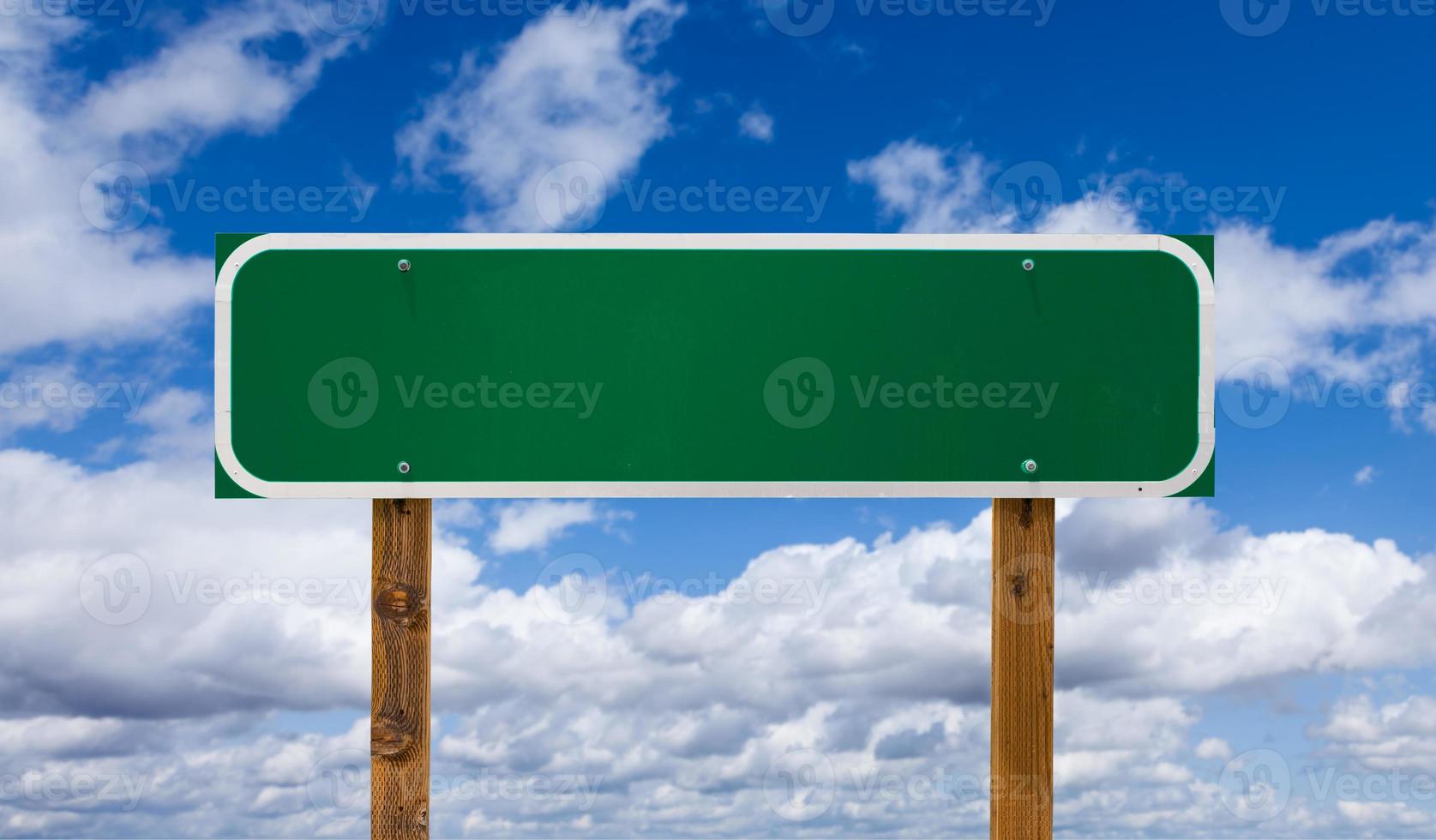 Blank Green Road Sign with Wooden Posts Over Blue Sky and Clouds photo