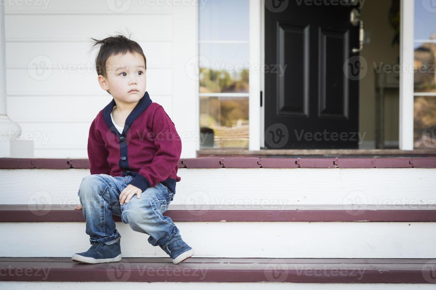 Melancholy Mixed Race Boy Sitting on Front Porch Steps photo