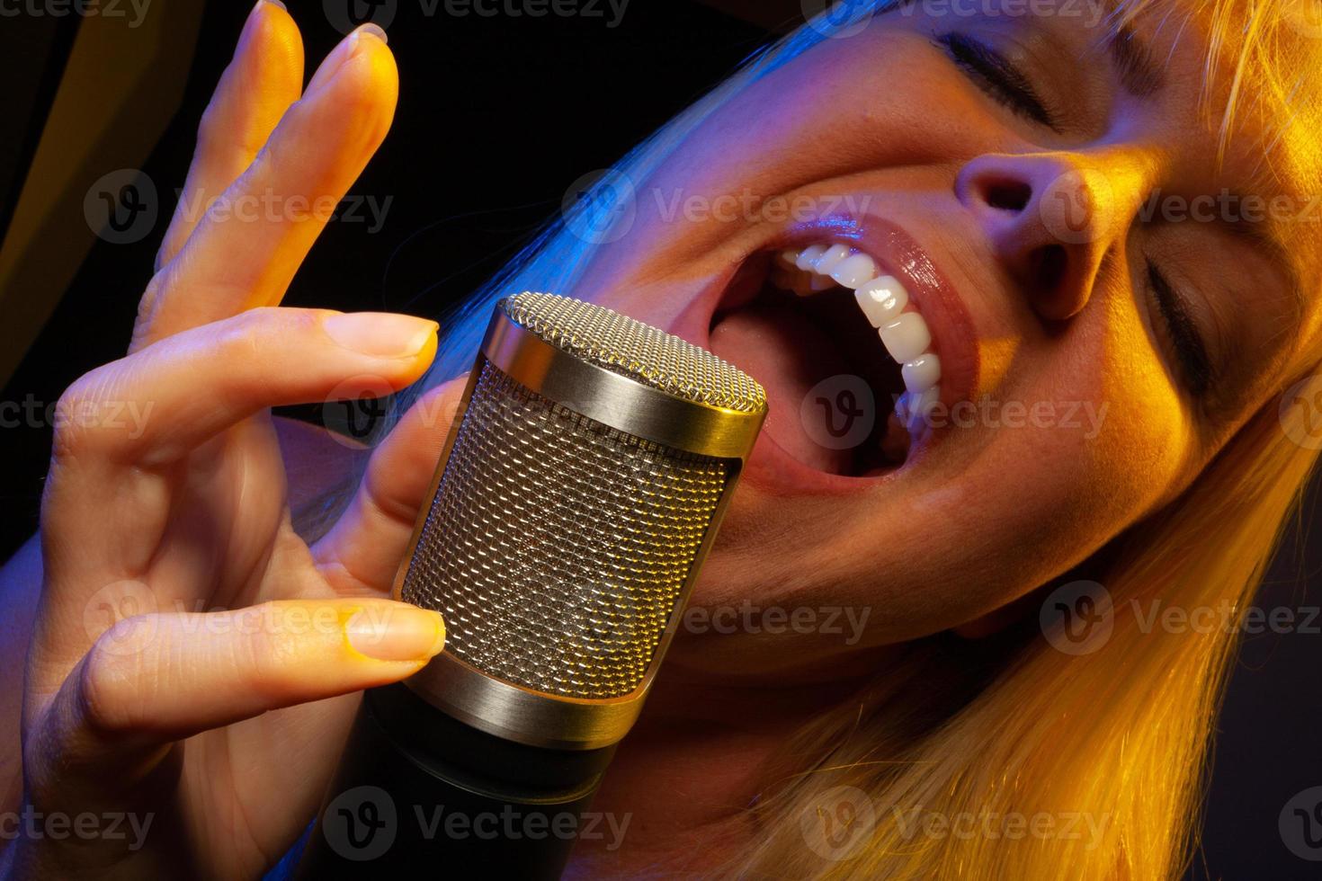 Female vocalist under gelled lighting sings with passion into condenser microphone. photo