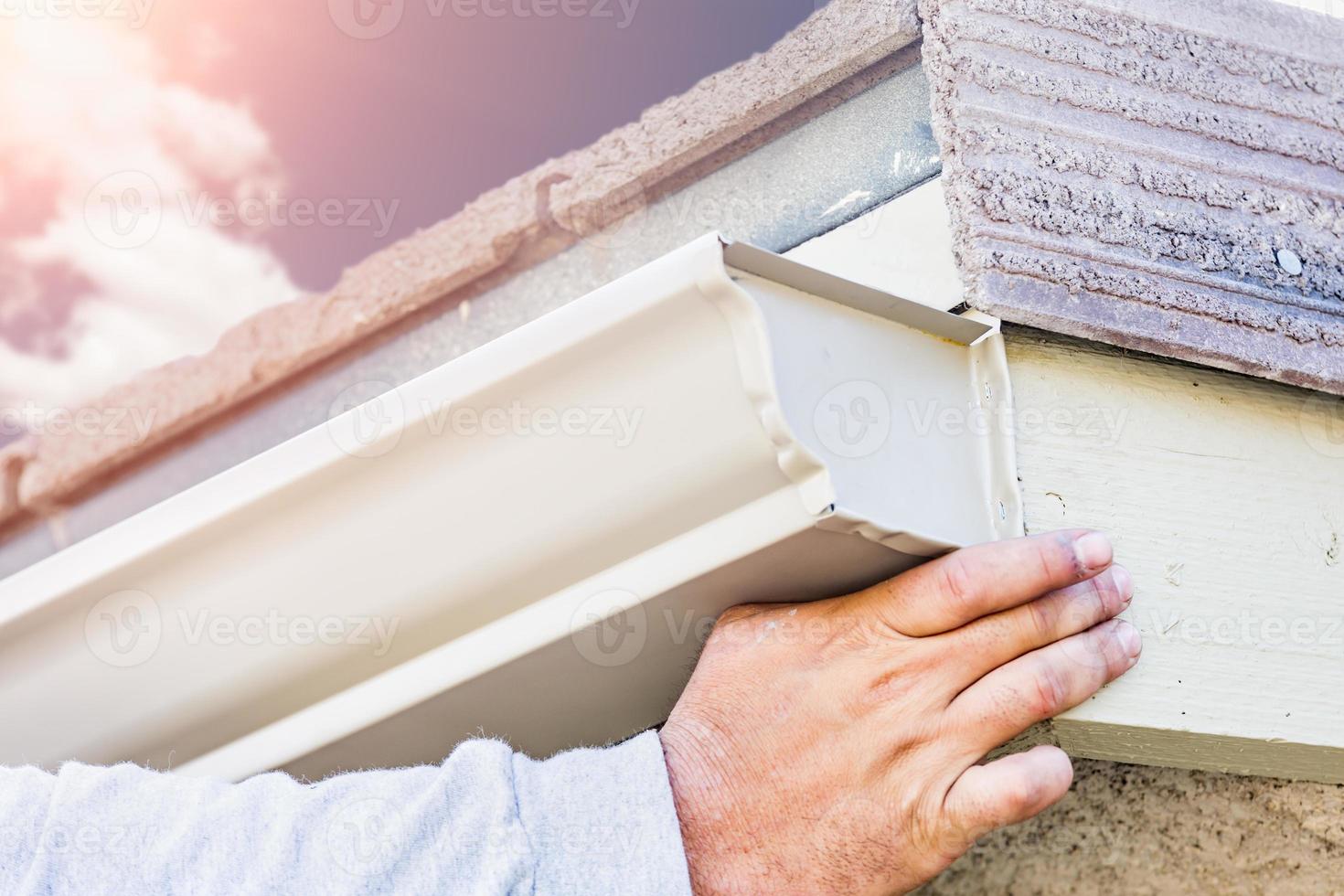 Worker Attaching Aluminum Rain Gutter to Fascia of House photo