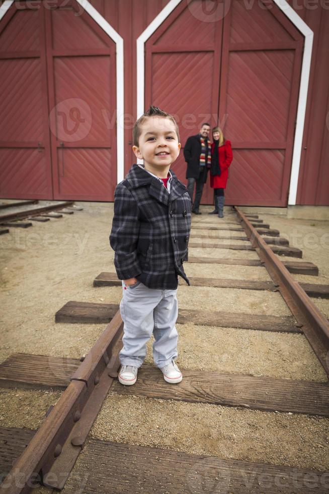 Mixed Race Boy at Train Depot with Parents Smiling Behind photo