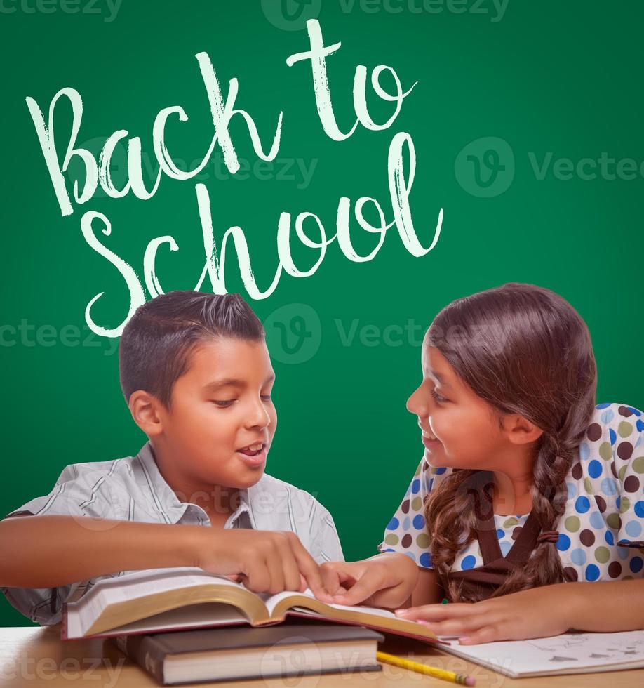 regreso a la escuela escrito en una pizarra detrás de un niño y una niña hispanos divirtiéndose estudiando juntos foto