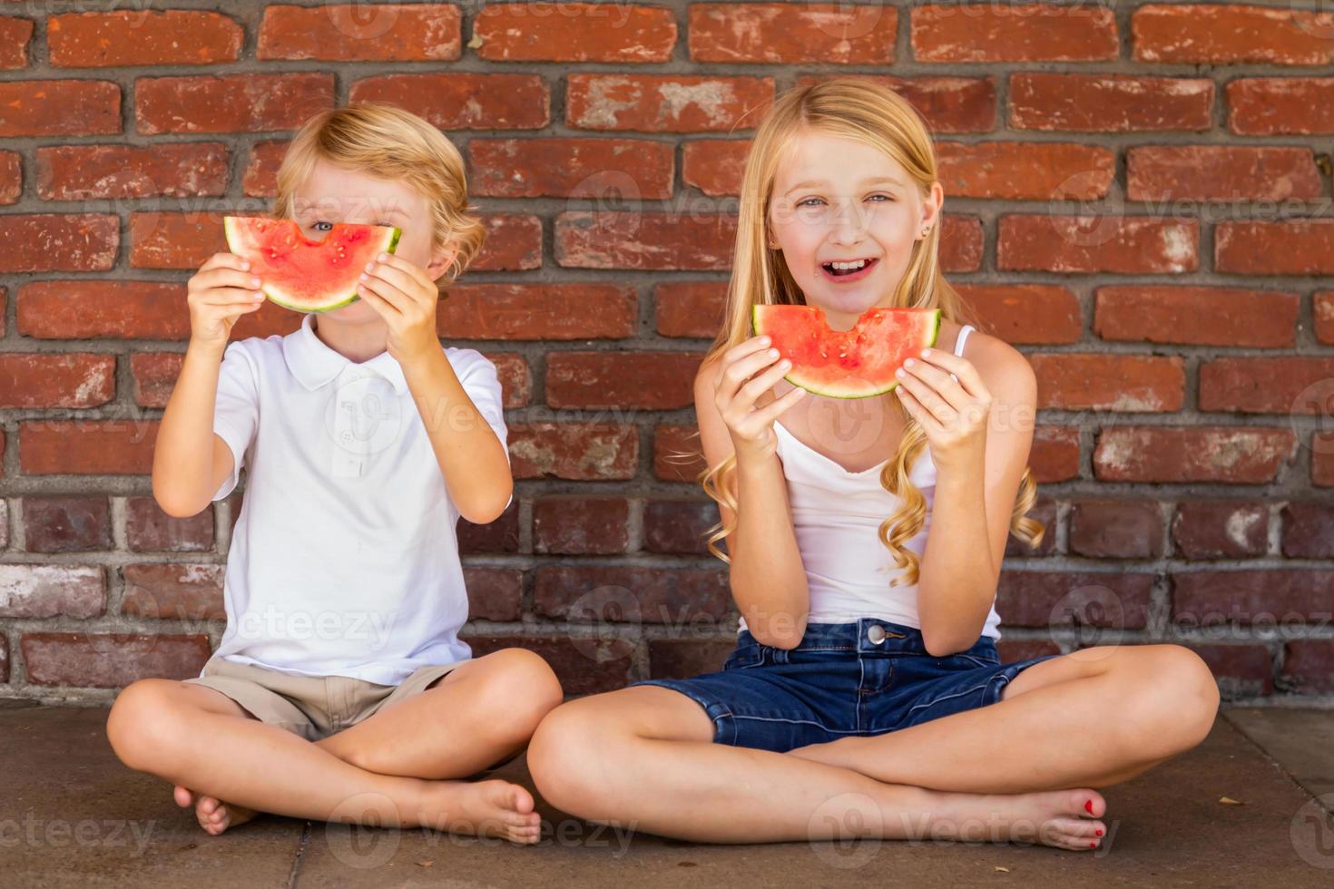Cute Young Cuacasian Boy and Girl Eating Watermelon Against Brick Wall photo