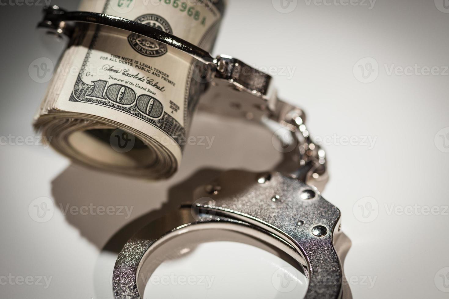 Handcuffs Locked on Roll of One Hundred Dollar Bills Under Spotlight photo