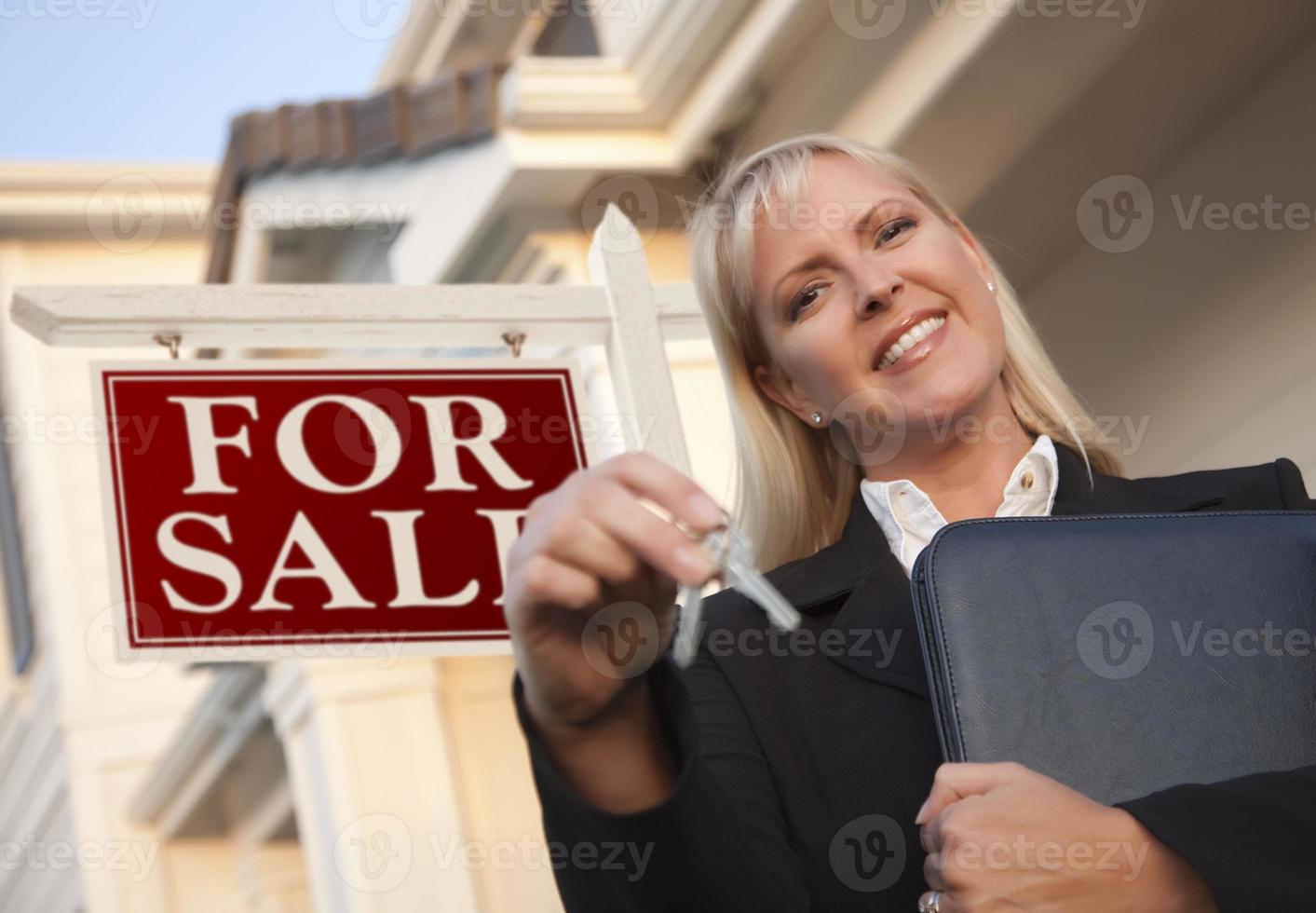 agente inmobiliario con llaves frente al letrero y la casa foto