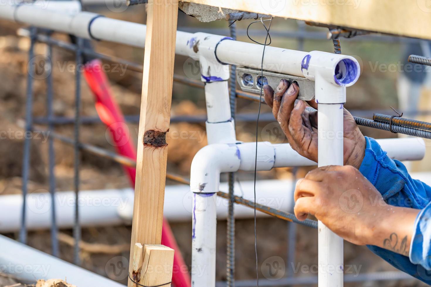 Plumber Using Level While Installing PVC Pipe At Construction Site. photo