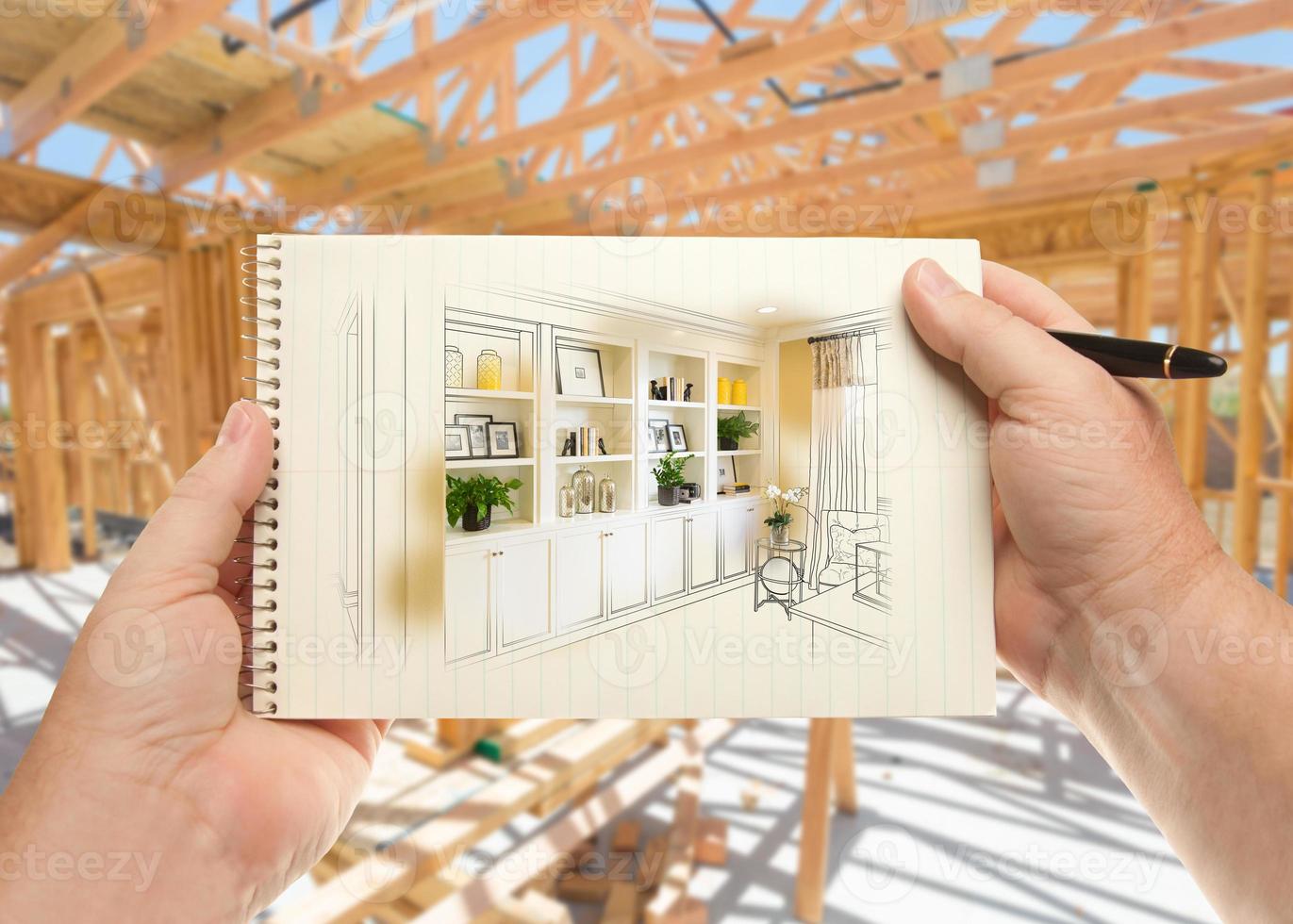 Hands Holding Pen and Pad of Paper with Built-in Shelves and Cabinets Inside House Construction Framing. photo