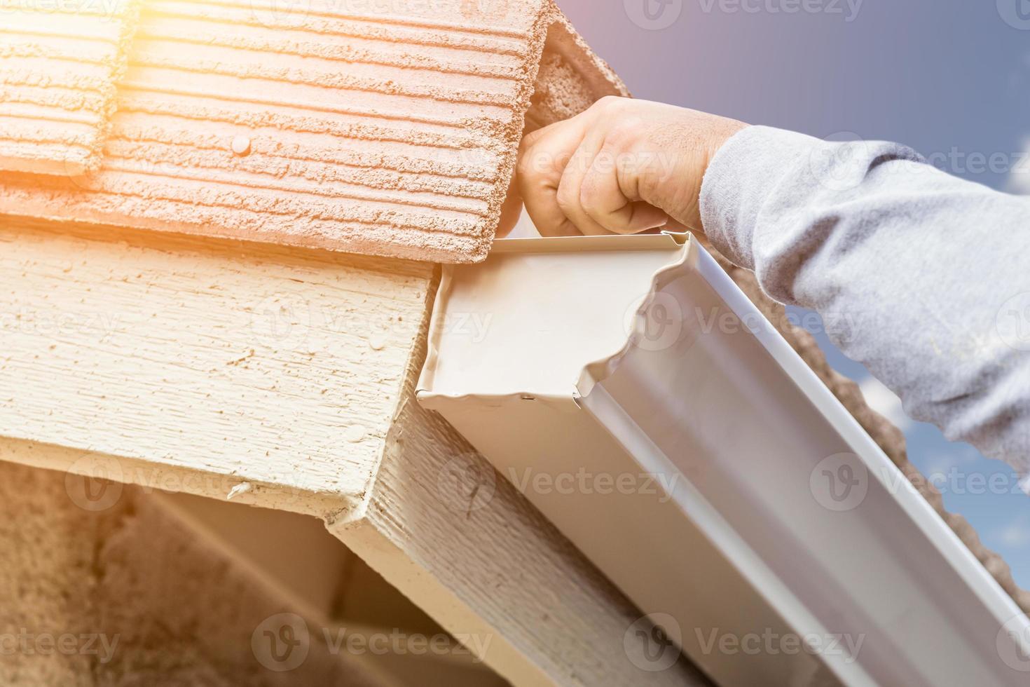 trabajador colocando un canalón de lluvia de aluminio en la fascia de la casa foto