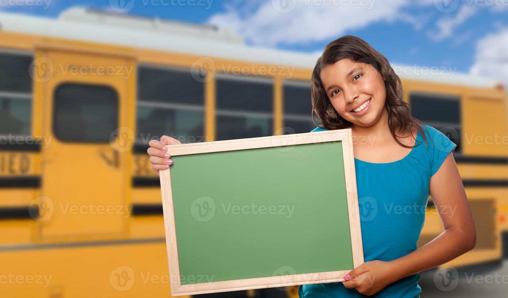 joven estudiante hispana con pizarra en blanco cerca del autobús escolar foto
