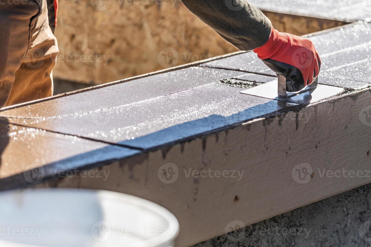 trabajador de la construcción que usa una bordeadora de acero inoxidable en cemento húmedo que forma una nueva piscina foto