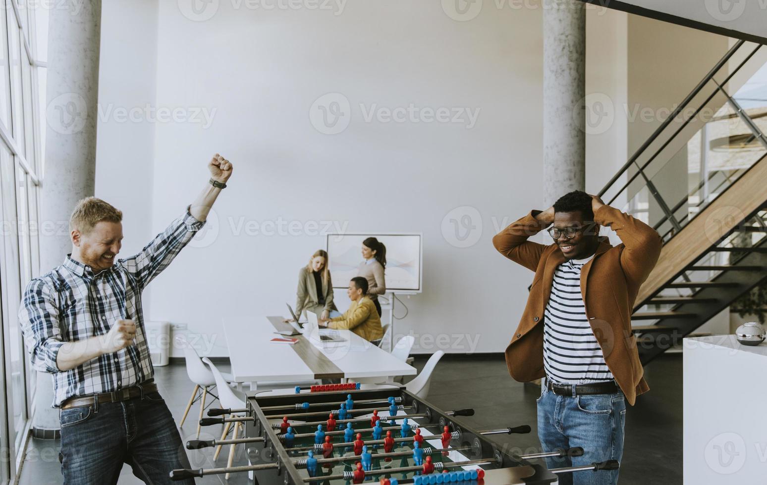 Young casual multiethnic business people playing table football and relaxing at office photo