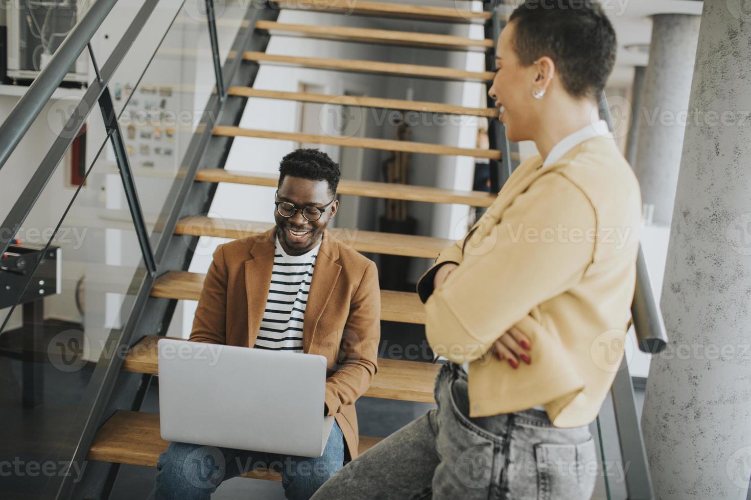 Young African American business man and short hair woman working on laptop while sitting at office stairs photo